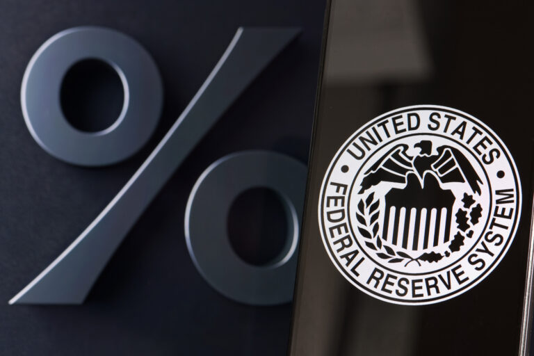 Fed logo displayed and sharp on smartphone screen in foreground, percent sign in background, interest rate regulation concept.